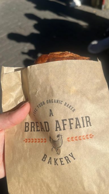 Eine Hand hält eine braune Papiertüte mit dem Aufdruck "A Bread Affair Bakery".