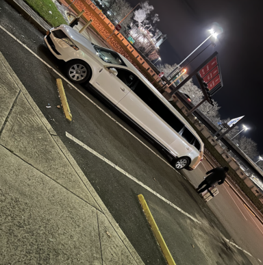 Weißer Stretchlimousine geparkt auf einem Parkplatz bei Nacht. Person geht vorbei.