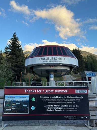 Rote Gondel mit informativem Schild vor einer Berglandschaft.