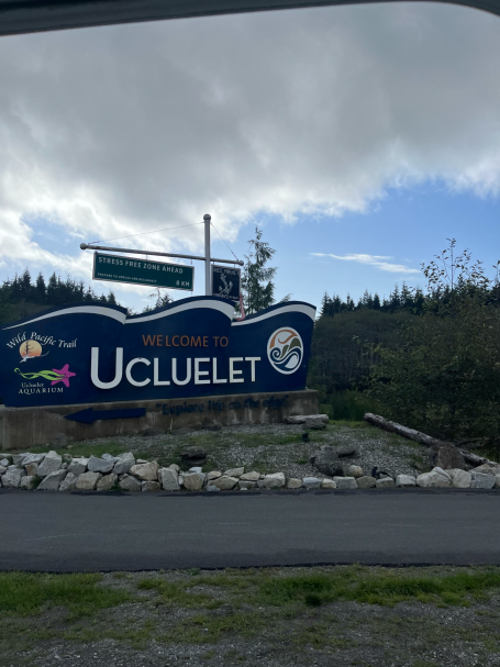 Willkommensschild von Ucluelet mit natürlicher Kulisse und bewölkten Himmel.