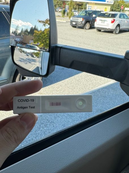 COVID-19-Test mit negativem Ergebnis, gehalten vor einem Autofenster.