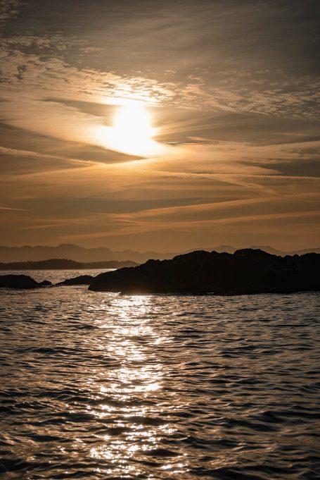 Sonnenuntergang über ruhigem Wasser, mit sanften Wellen und silbrigem Lichtreflex.