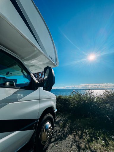 Ein Wohnmobil am Ufer unter einem klaren blauen Himmel, die Sonne strahlt.