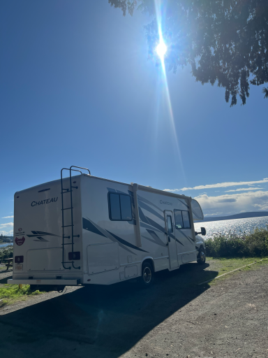 Wohnmobil parkt am Ufer, Blick auf das Wasser und strahlenden Sonnenschein.
