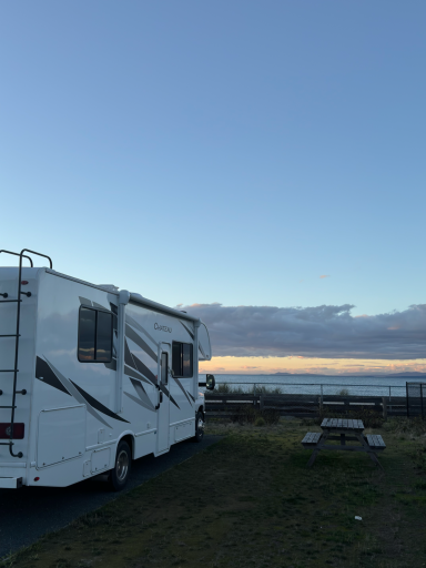 Wohnmobil steht auf einem Parkplatz mit Meerblick und Sonnenuntergang im Hintergrund.
