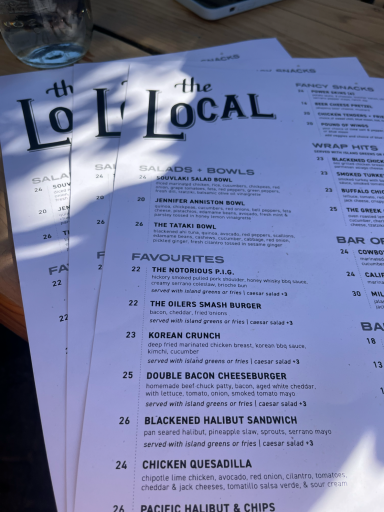 Speisekarte des Restaurants "The Local" auf einem Holztisch, mit Getränk im Hintergrund.