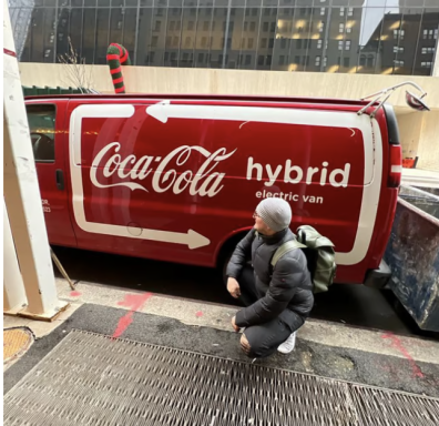Roter Coca-Cola-Transporter mit dem Schriftzug „hybrid“ und einer Person in squat-Position.