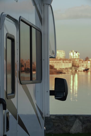 Wohnmobil mit Sicht auf die Stadt und den Spiegel einer ruhigen Wasseroberfläche.