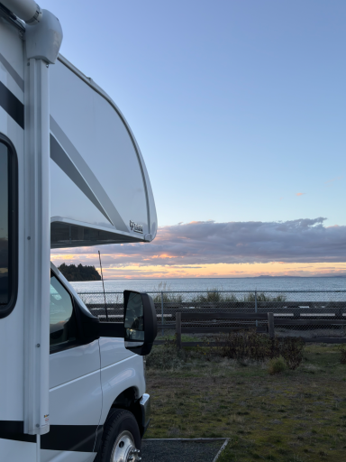 Wohnmobil an einem Strand mit Sonnenaufgang im Hintergrund.