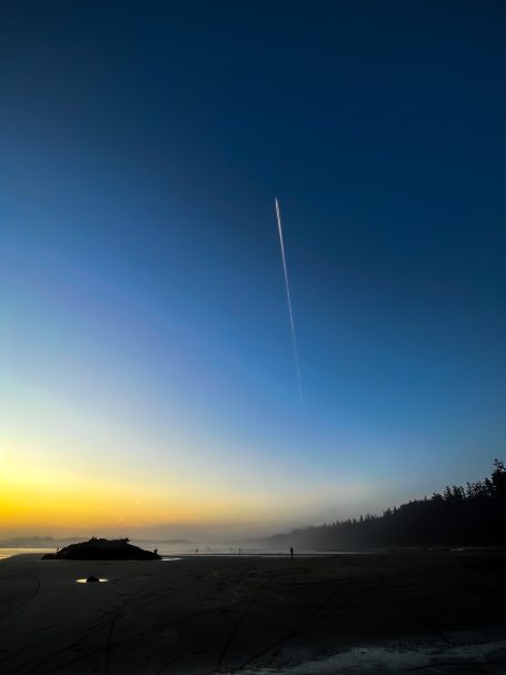 Sonnenuntergang über einem Strand mit einem Contrail am Himmel.