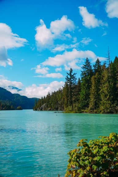 Ruhevoller See mit klarem, türkisfarbenem Wasser und umgebenden Wäldern unter blauem Himmel.