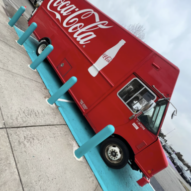 Roter Coca-Cola Lieferwagen parkt auf einer blauen Fläche.