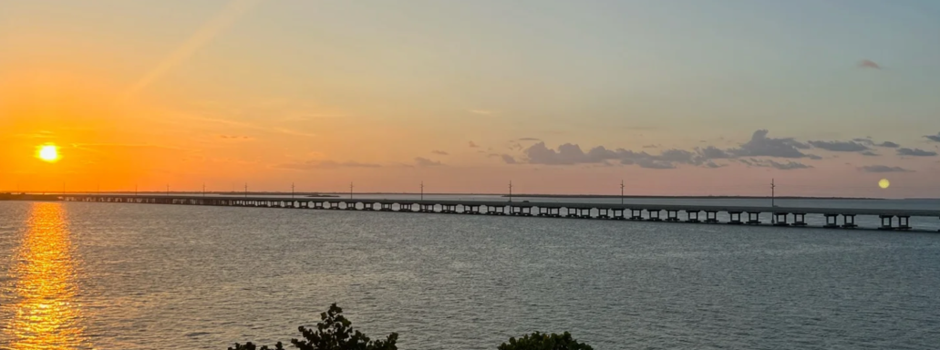 Sonnenuntergang über einem Wasserweg mit einer langen Brücke im Vordergrund.
