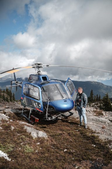 Blauer Hubschrauber steht auf felsigem Boden, ein Mann steht daneben.
