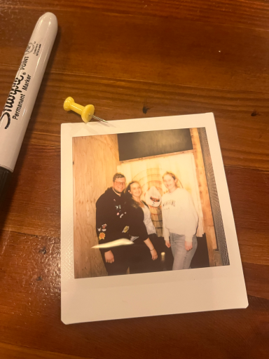 Vier Personen posieren lächelnd vor einem Hintergrund, mit einem Polaroid-Foto daneben.