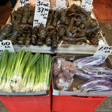 Lobster und frisches Gemüse wie Lauch und Auberginen auf einem Marktstand.