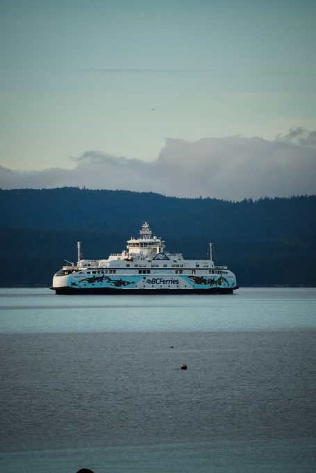 Fährschiff auf ruhigem Wasser mit Bergen im Hintergrund.