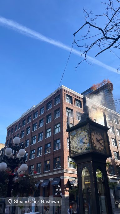 Historisches Gebäude mit einer großen, dekorativen Uhr im Vordergrund und klarem Himmel.