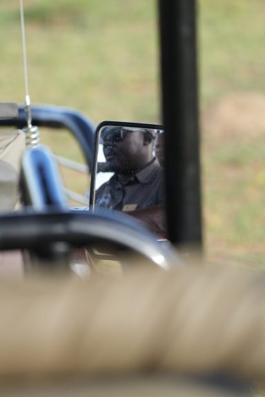 Ein Fahrer in einem Rückspiegel, mit Landschaft im Hintergrund.