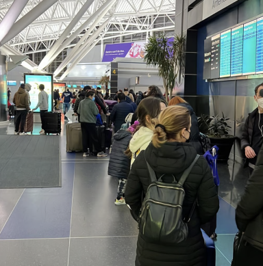 Menschen stehen in einer langen Schlange am Flughafen vor einer Anzeigetafel.
