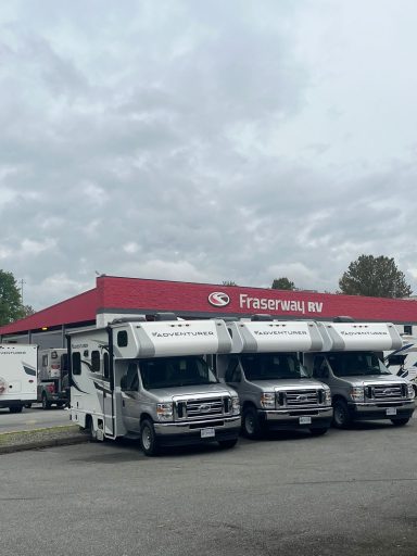 Drei Wohnmobile vor einem roten Verkaufsraum unter bewölktem Himmel.