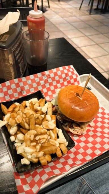 Burger mit orangefarbener Brötchenhälfte und Pommes frites auf einem karierten Tisch.