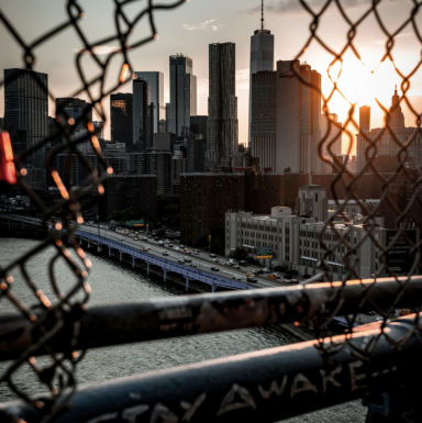 Blick auf die Skyline von New York City bei Sonnenuntergang durch einen Maschendrahtzaun.