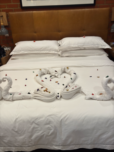 Zwei gefaltete Handtücher in Form von Schwänen auf einem Bett mit Blumenblättern.