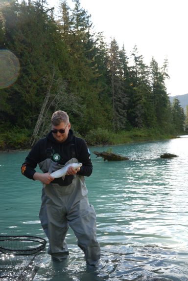 Eine Person in Wathose steht im Wasser und hält einen Fisch mit beiden Händen.