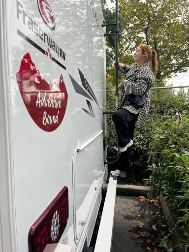 Junge Frau klettert an einem Lieferwagen hoch, um eine Möglichkeit zu erreichen.