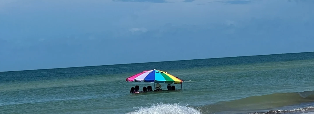 Bunt gestreifter Sonnenschirm am Strand mit Wellen im Meer im Hintergrund.