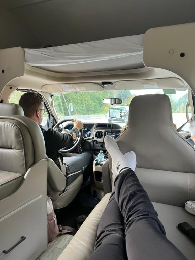 Person fährt einen Van, Füße liegen entspannt auf dem Sitz.