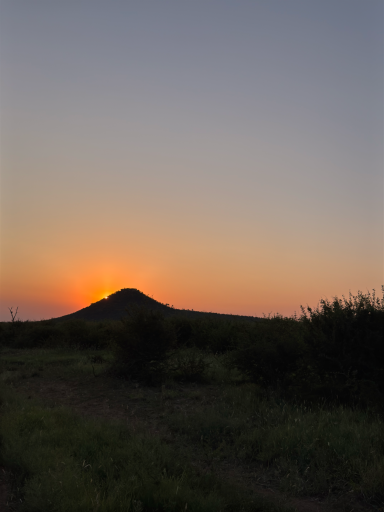 Sonnenuntergang hinter einem Hügel, sanfte Farben am Himmel und dunkle Silhouetten.