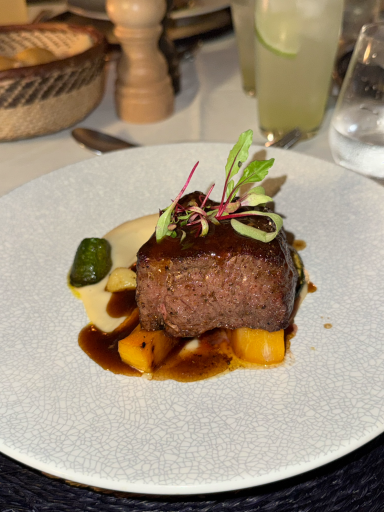 Rindfleischstück mit Sauce, Gemüsebeilage und Garnitur auf einem weißen Teller.