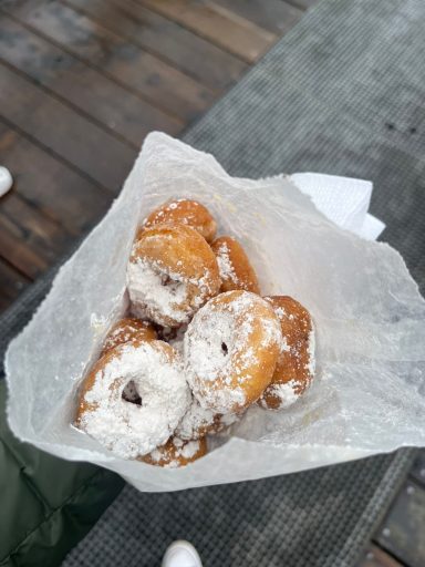 Drei frisch zubereitete, pudergzuckerte Donuts in einer Papierverpackung.