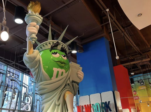 Eine grüne M&M-Figur als Statue of Liberty in einem bunten Raum.
