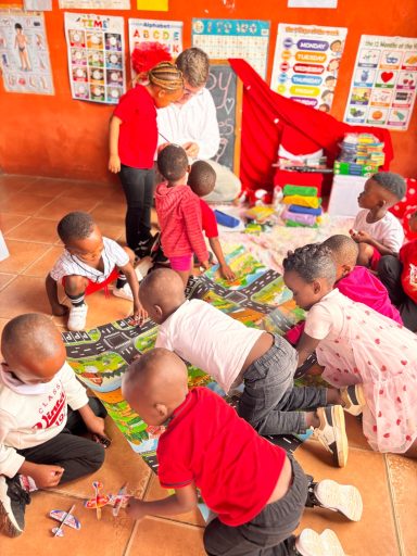Kinder sitzen auf dem Boden und spielen mit bunten Spielmaterialien in einem Klassenraum.