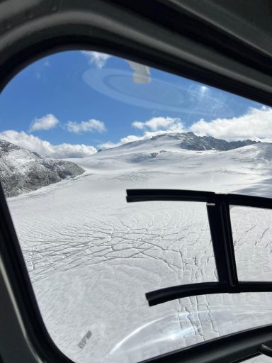 Blick aus einem Fahrzeugfenster auf einen schneebedeckten Gletscher unter blauem Himmel.