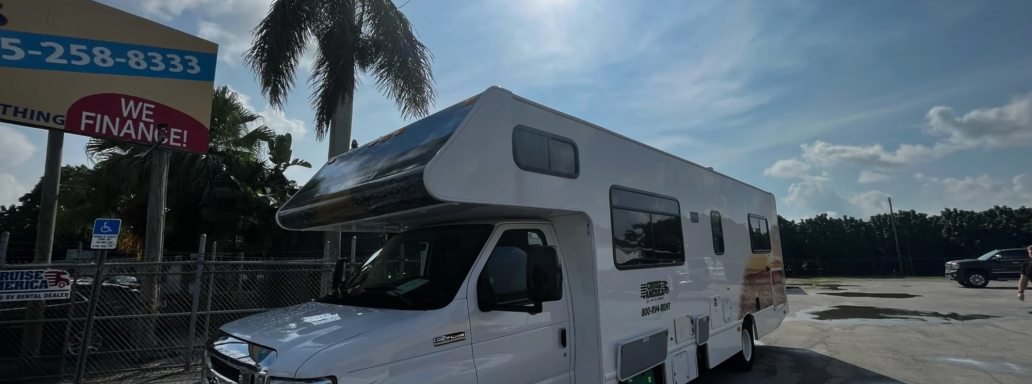 Ein Wohnmobil parkt unter einem sonnigen Himmel mit wenigen Wolken.