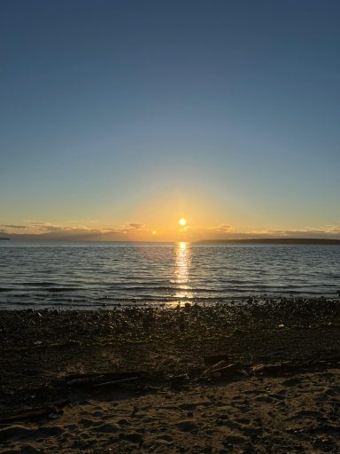 Sonnenuntergang über dem Wasser mit reflektierendem Licht und ruhiger Küstenlinie.